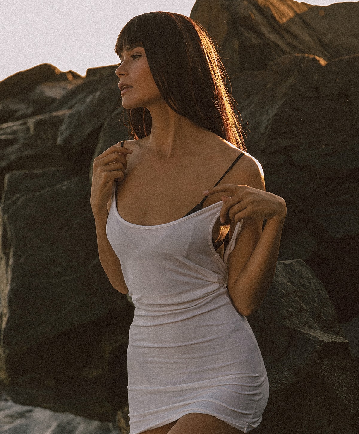 Woman in a white dress by rocky shoreline.