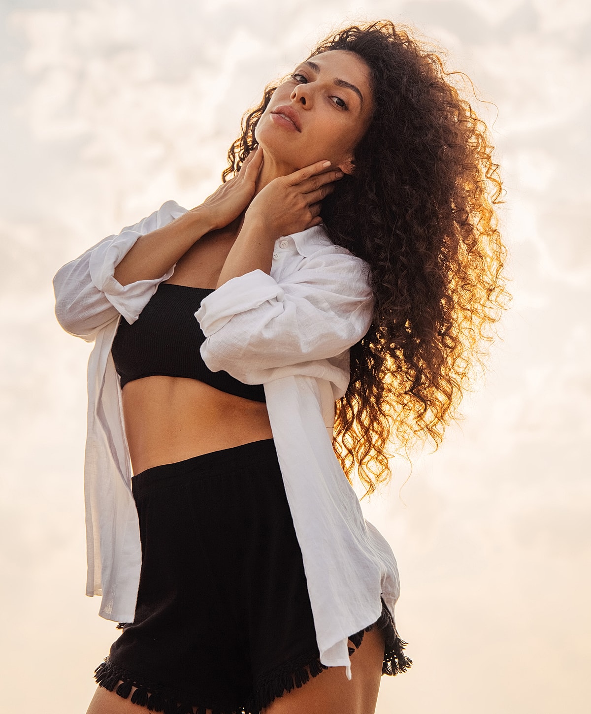 Woman with curly hair in sunlit outdoor setting.